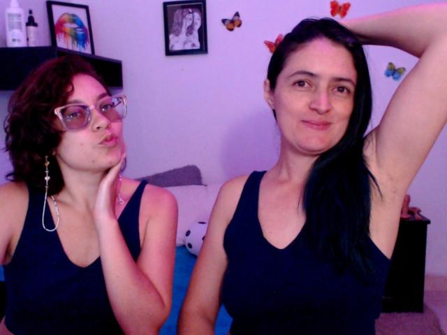 LunaVenus with curly brown hair and glasses, pouting, has small tits and wears a black tank top. LunaVenus with black hair, arm raised, has medium tits and wears a tank top.