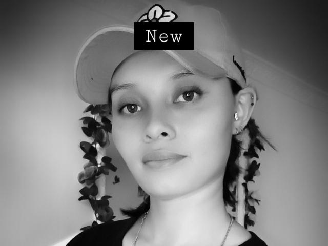 Black-and-white photo of Ahllana with a cap, leaf vines in her hair, and a serious expression, showing small earrings and a necklace. Her tits are not visible.