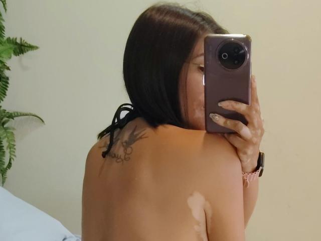 SharissWilliam taking a mirror selfie, topless, showing a tattoo on her right shoulder blade, holding a purple phone, with a pink watch on her left wrist.