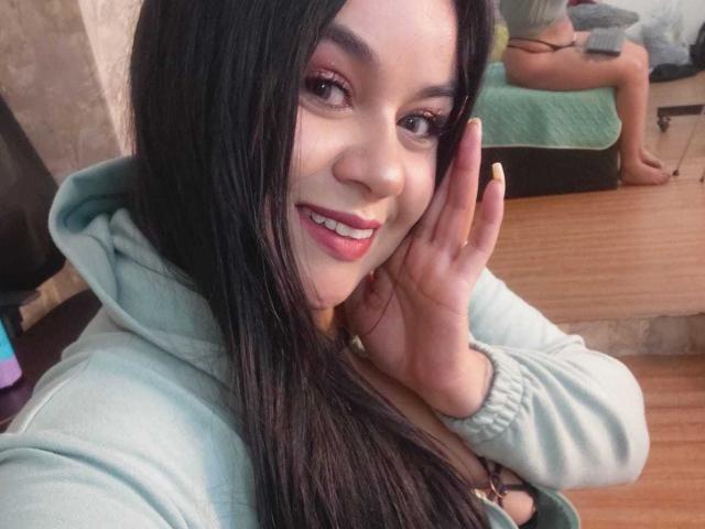 EveWillis with long black hair, pink eyeliner, smiling, wearing a green hoodie, touching her cheek, mirror reflection showing her bare ass.