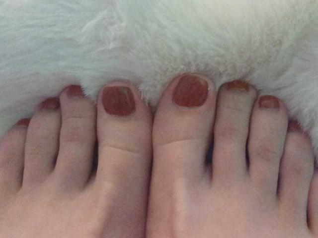 KatalinaLaurent's bare feet are positioned with soles touching, showing slightly pink toes and visible veins on a textured, light-gray carpet.