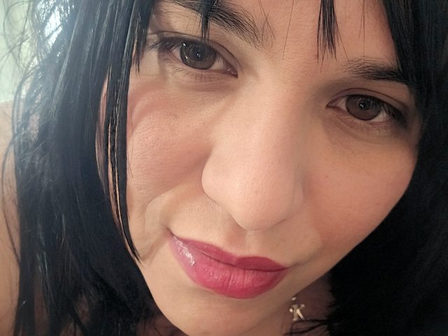 VivianaThomson's face, showing dark brown eyes, pink glossy lips, and black straight hair with bangs. She's wearing a necklace, and her skin is light with slight wrinkles.