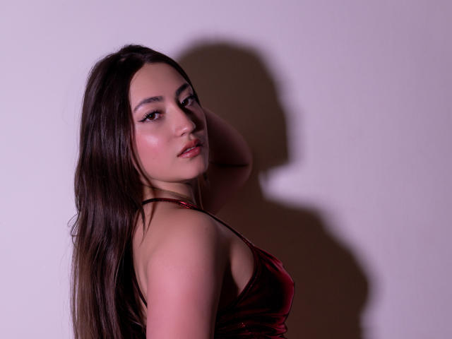 AnnFisher with long brown hair, wearing a red velvet halter top, looking over her shoulder, hand behind her head, showing her ass, with pink eyeshadow and subtle blush.