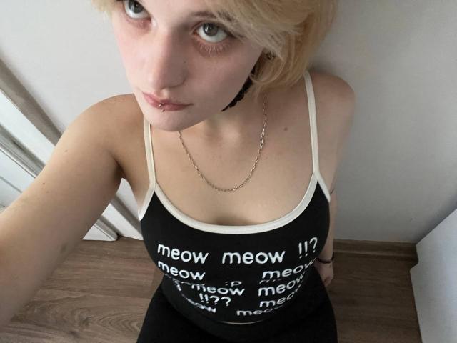 AnnaCandys has short blonde hair, pale skin, and a lip piercing. She's wearing a black tank top and a chain necklace, with small tits and a cute face.