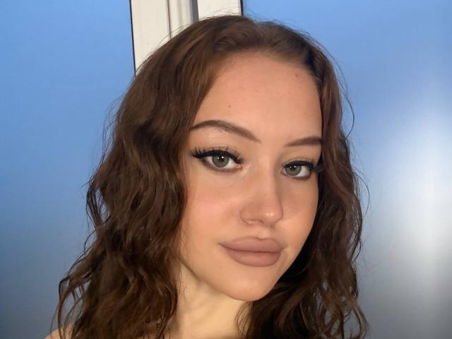 MicheleJinkins has wavy brown hair, green eyes, and full lips with nude makeup. She's looking slightly to the side with a subtle smile. Her ass is not visible.