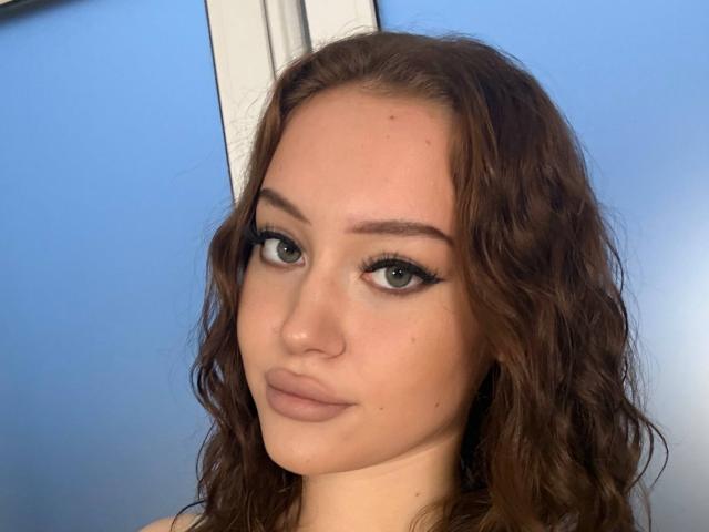 MicheleJinkins has wavy brown hair, light skin, and is wearing bold black eyeliner with long lashes. She's looking at the camera with a slight, neutral smile.