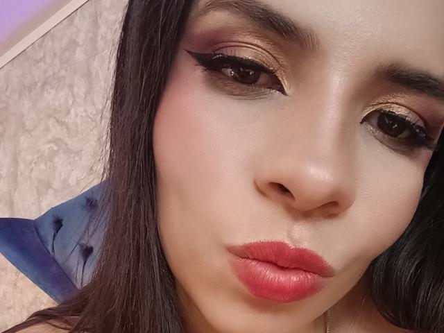 VioletaStone has glossy brown eyes with thick black eyeliner, gold shimmer eyeshadow, and red lipstick. Her pouty lips are slightly parted, and she has smooth, light skin.