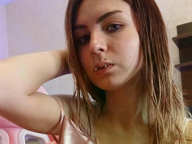 NobukoGraue has wet brown hair, blue eyes, and multiple nose piercings, including a septum ring and a lip piercing. She's looking at the camera with a slight pout.