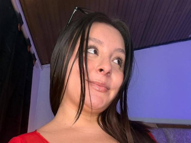 EmaJames has long black hair, a cute smile, and a slightly mischievous look with her lips puckered. She's wearing a red shirt, and her eyes are looking sideways.