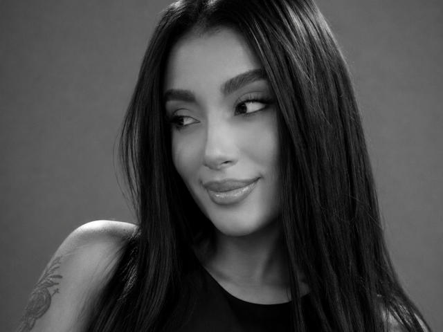 CristalRousse has long, straight black hair, dark eyebrows, and a subtle smile. She's looking to the side with glossy lips and a tattoo on her right shoulder.