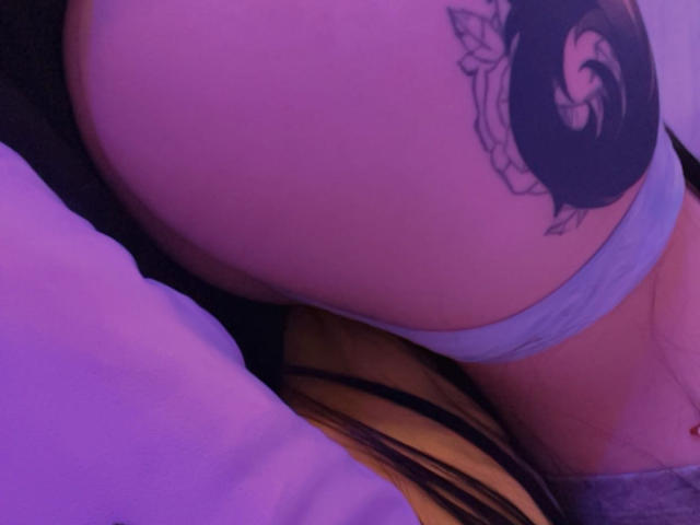I glutei di AizenMyoo in biancheria intima azzurra, con un tatuaggio di una rosa nera sul lato destro, illuminati da luci viola. Si vede un tessuto giallo e nero a righe..