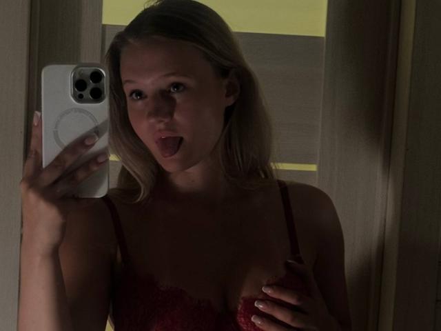 Shonna Sjolund, avec ses cheveux blonds, un soutien-gorge en dentelle rouge, tenant un téléphone, la langue tirée, une main sur ses seins, éclairage tamisé, reflet dans un miroir, iPhone avec une coque blanche..
