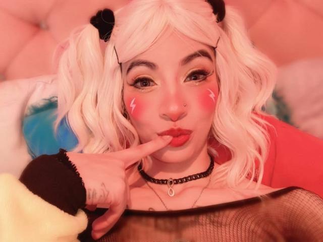LaurenEvie69 with white pigtails, black horns, red lipstick, and pink blush, sucking on a finger, wearing a black choker and fishnet top, showing a cute, sexy face.