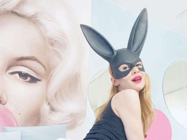 RebelLuna with blonde hair, wearing a black bunny mask and black tank top, has pink lipstick and is looking at the camera. A Marilyn Monroe face is on the left.