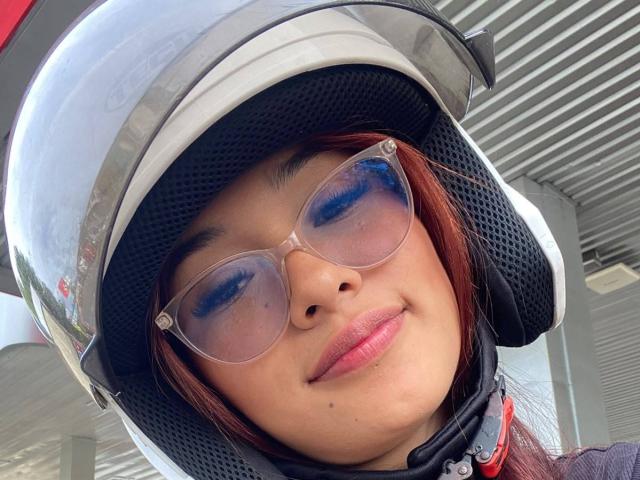 SashaHans with red hair, wearing a clear helmet, blue-tinted glasses, and a slight smile, showing off her cute ass with a black mesh helmet covering.
