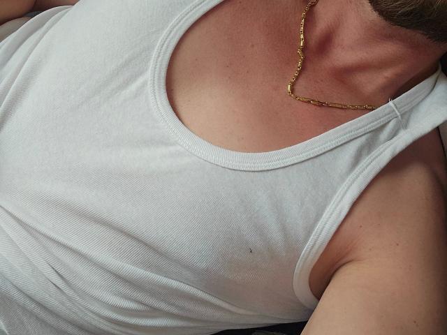 La canotta bianca di Johny13313-hot mette in mostra il loro seno, con una collana d'oro e i segni della abbronzatura sul petto. Si vede un braccio sul lato destro..