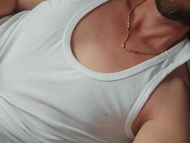 Johny13313-hot's chest in a white tank top, showing a tan line and a gold necklace, with a visible collarbone and part of a beard.