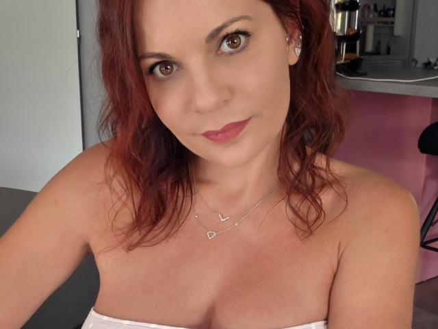 JuneLaFrenchie heeft rood haar, bruine ogen en roze lippenstift. Ze draagt een witte top zonder bandjes, waardoor haar borsten zichtbaar zijn, en een zilveren ketting met een klein hartje eraan..