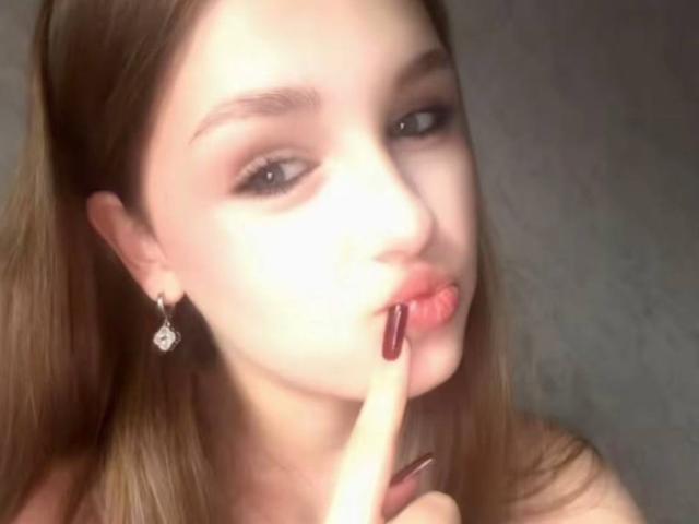 MelisaMagnie with light brown hair, pink lips, and dark red nail polish, sucking on her index finger, showing off her diamond earrings, with a soft, glowing face.