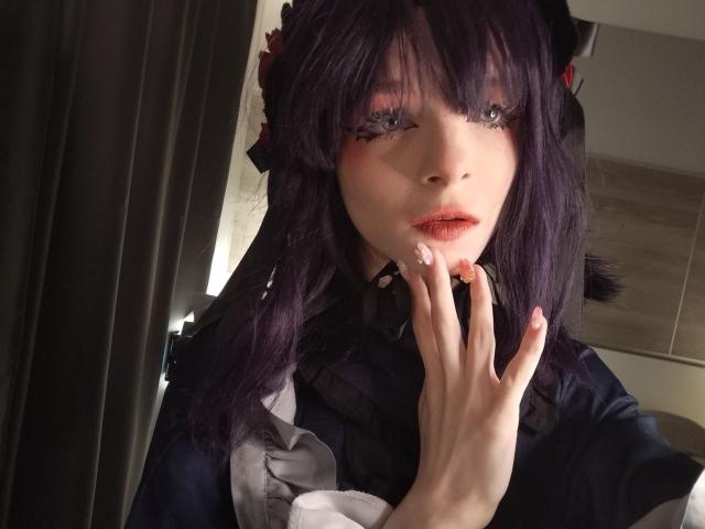 ChangCaddle with purple hair, wearing a black and grey outfit, touching her lips with a hand, has pink eyeliner and red lipstick, looking seductive with half-closed eyes.