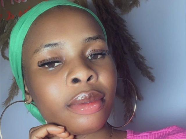 Nastybitch-hot has dark brown skin, green headwrap, and large hoop earrings. She's sticking out her glossy pink lips with half-closed eyes and long eyelashes.