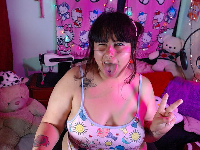 LilithHeavy with big tits, purple tongue, and tongue piercing, wearing sun-themed tank top, making peace sign, glasses, and headphones, pink and purple lighting, brown hair, tattoos.