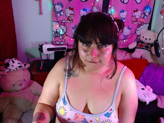 LilithHeavy with dark brown hair in a bun, wearing a sun and butterfly print bra, clear face mask, and headphones, has tattoos, medium tits, and a slight smile.