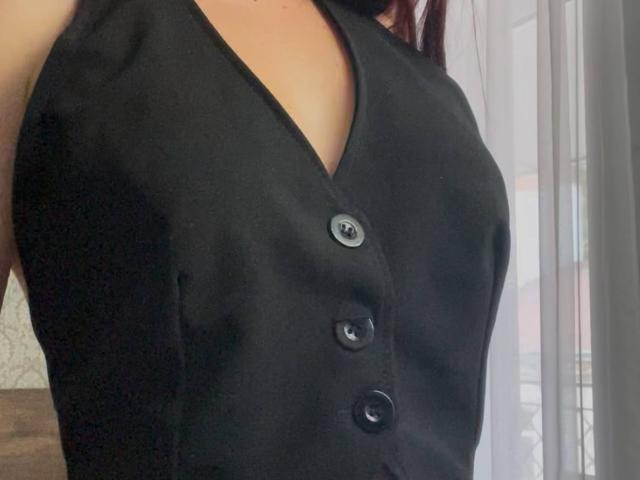 AlexXas' black sleeveless vest with a v-neck and three buttons, showing her small, perky boobs and a bit of her cleavage. Her arm is slightly raised.