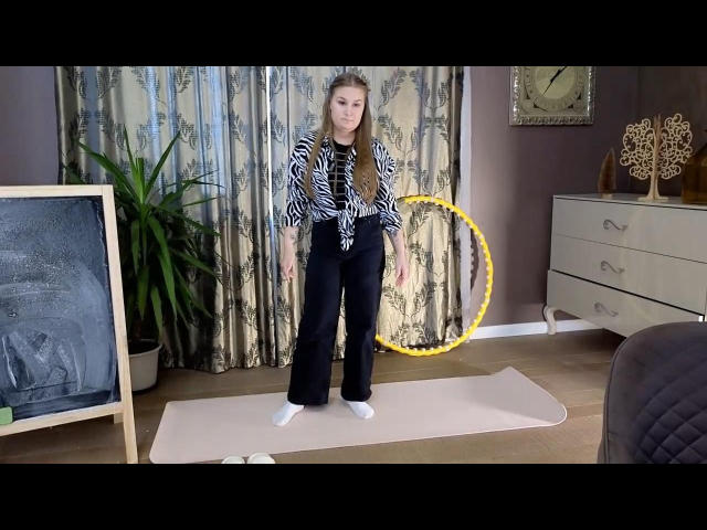 ValerieSchultheiss stands on a pink mat, wearing a zebra print shirt, black pants, and white socks. Yellow hula hoop, potted plant, and dresser in the background.