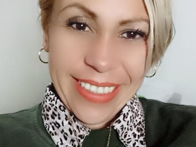BiancaVelvet has blonde hair, hoop earrings, and is smiling with red lipstick. She's wearing a green shirt with a leopard print collar. Her tits are not visible.