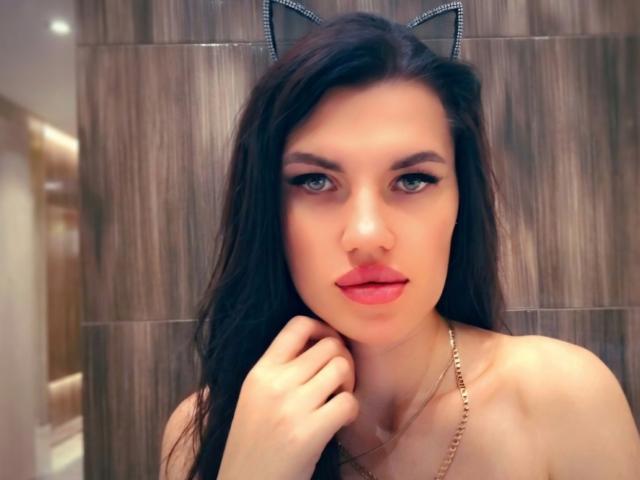 MilaLoona with cat ears, long dark hair, green eyes, red lipstick, hand on chin, gold necklace, looking at camera, wooden wall background, soft lighting, slightly parted lips.