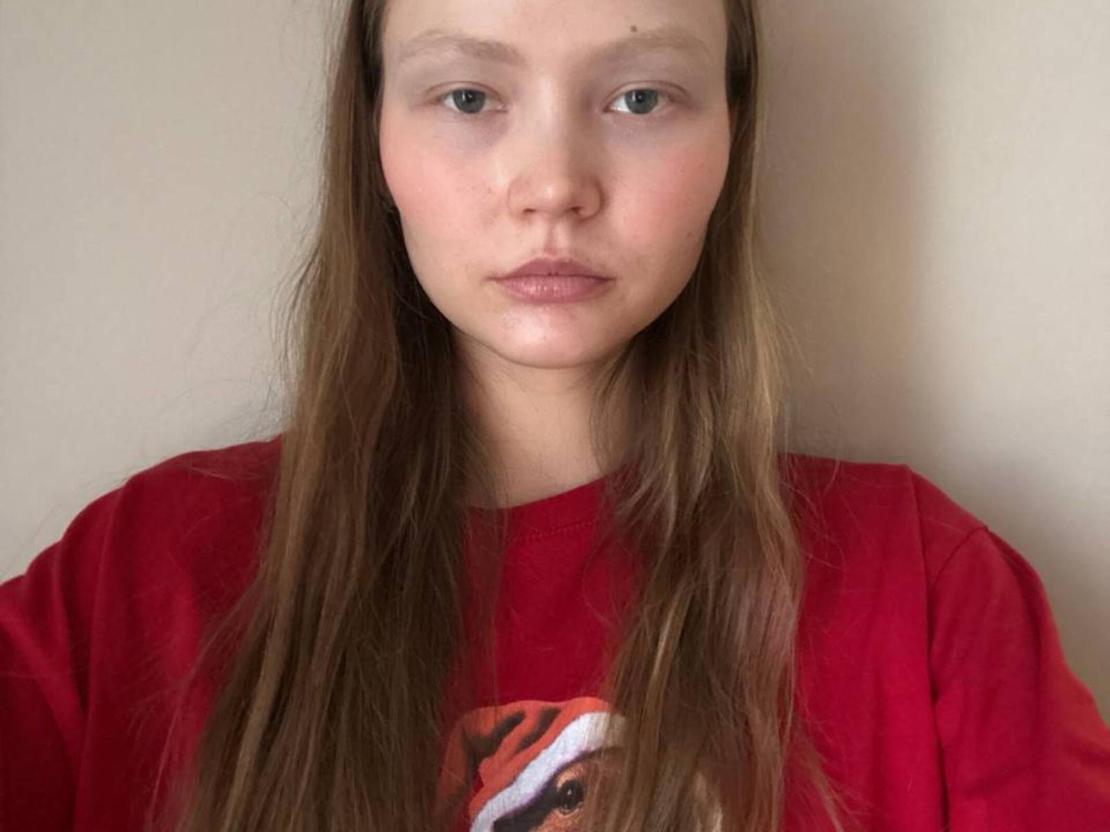 Eula Yanek hat braunes, glattes Haar, helle Haut und grüne Augen. Sie trägt ein rotes Hemd mit einem Teilmuster und blickt direkt in die Kamera, wobei sie einen neutralen Gesichtsausdruck hat..