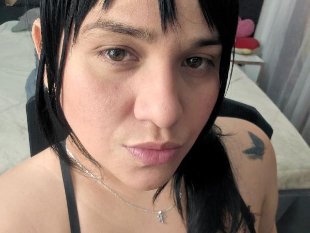 VivianaThompson has black hair, brown eyes, and a butterfly tattoo on her right shoulder. She's wearing a black top, a silver necklace, and has pink lips.