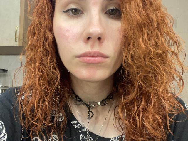 Ivelisse Buol ha i capelli rossi ricci, la pelle chiara e l'eyeliner nero. Indossa una collana nera con un dente di serpente e una camicia nera con un motivo, e ha un'espressione accigliata..