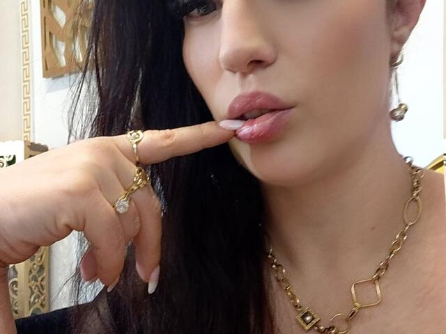 VanessaSquirtt's face, finger with gold ring and diamond, touching pink lips, wearing gold chain necklace, black hair, subtle makeup, pink lipstick, slightly parted lips.