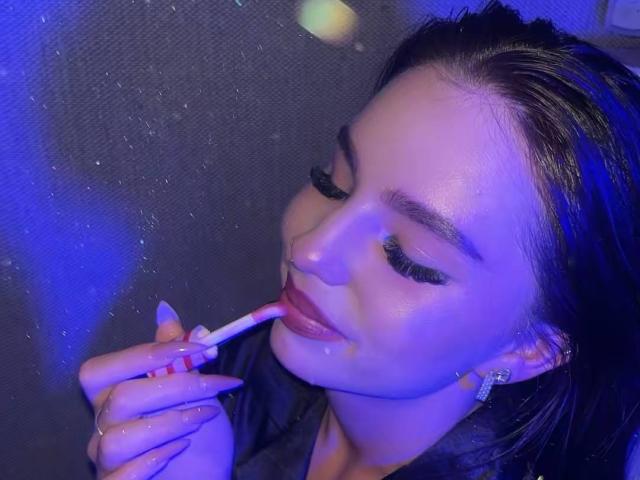 MarquitaVoltz with glossy brown hair, applying pink lipstick, eyes closed, long black eyelashes, subtle blue lighting, holding lipstick, earrings, slightly parted lips, subtle smile, soft skin.