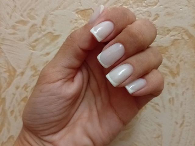 ViktoriiaLu's hand with glossy white nail polish on medium-length, square-shaped nails. Her skin is light brown, and she's holding her hand slightly curled.