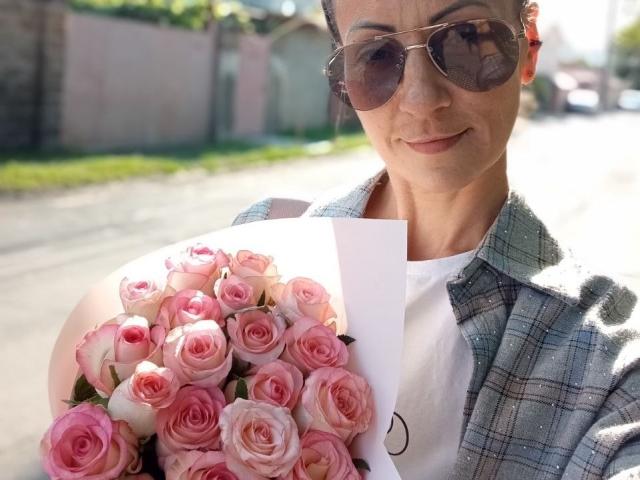 ViktoriiaLu with pink roses, wearing sunglasses, a plaid shirt, and white tee, holding bouquet in sunlight, smiling. Her tits are small, face is pretty, she's hot.