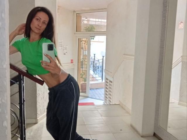 ViktoriiaLu with slim, flat-ass, and small tits, wearing a green crop top and black track pants, taking a mirror selfie in a white hallway.