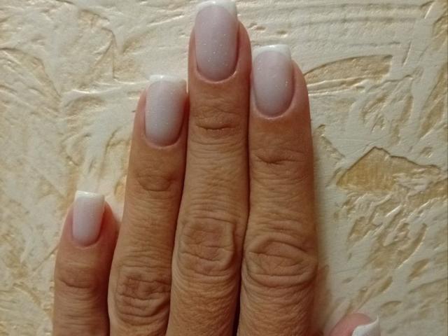 ViktoriiaLu's fingers with her manicured nails, featuring glossy white polish, are shown against a textured, beige wall. Her nails are neatly trimmed and slightly curved.