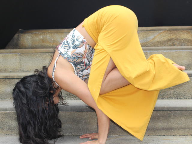 LucyySky is bending over with her ass up, wearing a floral top and yellow skirt, exposing her pussy and her black curly hair is in her face.