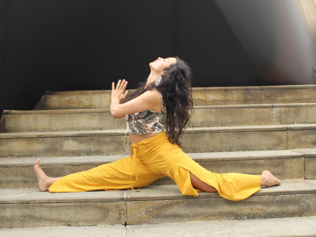 LucyySky with long dark hair, sleeveless top, and yellow pants, stretching on concrete stairs, head back, eyes closed, hands up, legs spread, barefoot, looking relaxed and graceful.