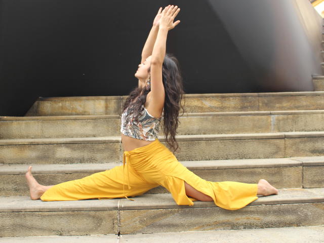 LucyySky, split down the middle, arms raised, wearing a leaf-patterned top and yellow pants, showing her tits and ass, barefoot on concrete steps, in a yoga pose.