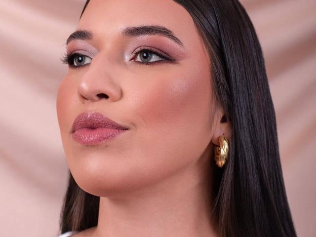 O rosto de Rachel Wilson, olhando para cima com sombra rosa, batom rosa brilhante e um brinco de argola dourado em cabelos pretos lisos, exibindo uma pele lisa e levemente avermelhada..