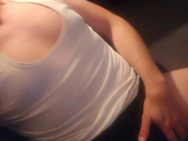 La canotta bianca di Johny13313-hot, che mostra i suoi seni, leggermente trasparenti, con una mano sulla zona inguinale, biancheria intima nera e un braccio sollevato, in una foto ravvicinata e con scarsa illuminazione..