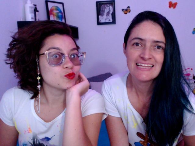 LunaVenus with curly brown hair, glasses, and red lipstick, making a pouty face, next to LunaVenus with straight black hair, smiling, wearing white shirts with colorful splashes.