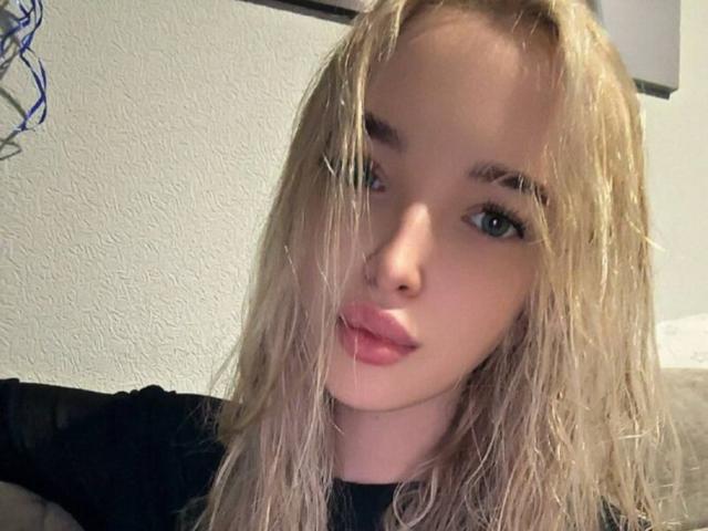 BrookeZapf, blonde, avec les cheveux mouillés et en désordre, les lèvres pleines et roses, et les yeux bleus, portant une chemise noire, dans un autoportrait. Ses seins ne sont pas visibles. Elle a l'air mignonne..