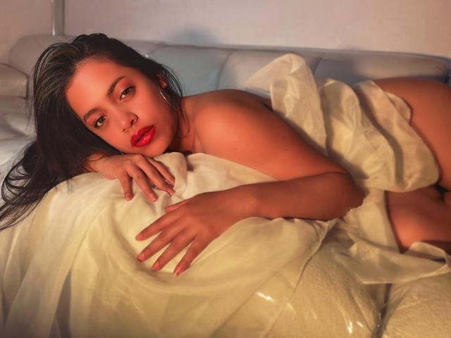 Grace Cooper è sdraiata su un letto con lenzuola bianche, le sue labbra rosse e i capelli scuri contrastano con la sua pelle abbronzata. Il suo seno è parzialmente coperto, i suoi glutei sono per lo più nascosti..