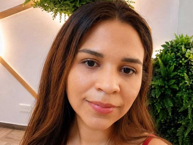 Zephyra Belmont tem cabelo castanho, olhos castanhos e um tom de pele claro, com um sorriso discreto. Ela está vestindo uma blusa vermelha, e suas nádegas não estão visíveis..