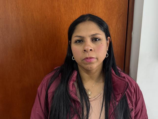 AndrexMilf has black hair, brown eyes, and a pensive look. She's wearing a pink shirt, small earrings, and a necklace with a heart pendant. Her face is slightly chubby.